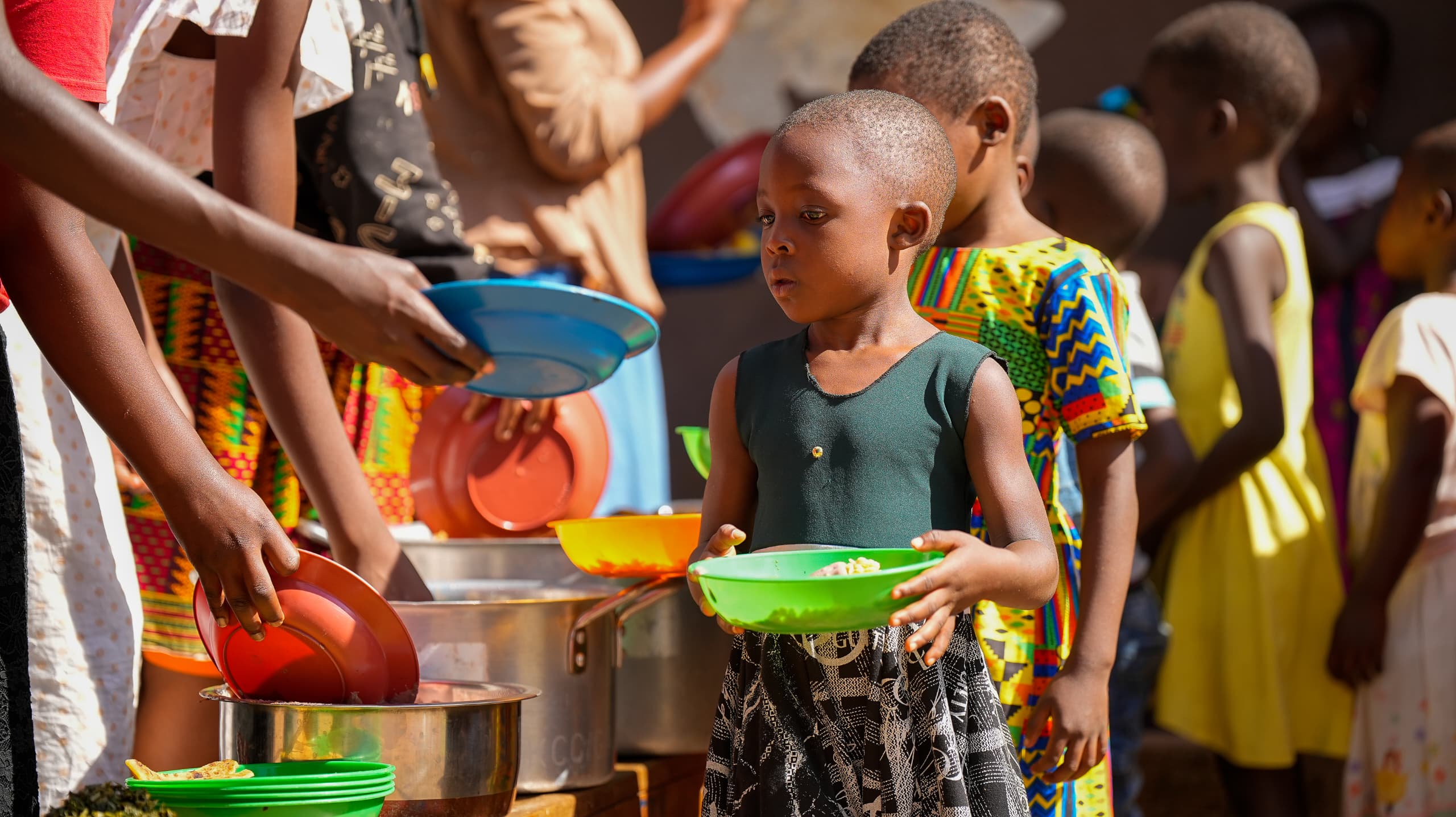 A young girl holding a bowl of food at a feeding day in Kivulu